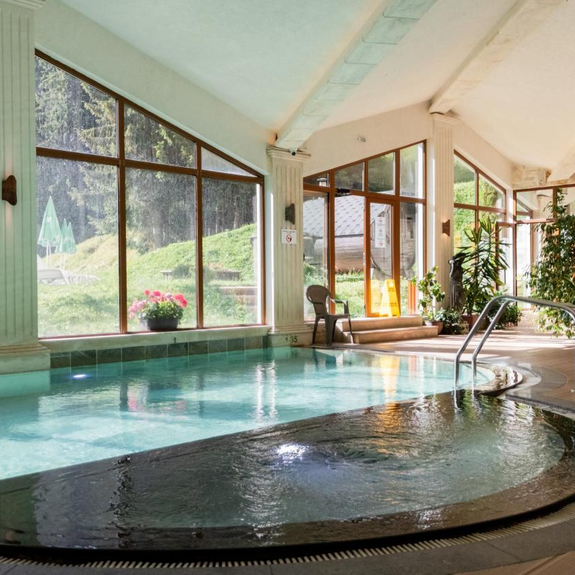 An indoor swimming pool with large windows, a chair, and a plant.
