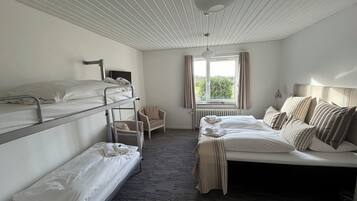 Et sovesal med køjesenge, en enkelt seng, en stol, en radiator og et vindue med gardiner.