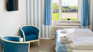 A hotel room with a bed, a chair, a TV, and a window with curtains.