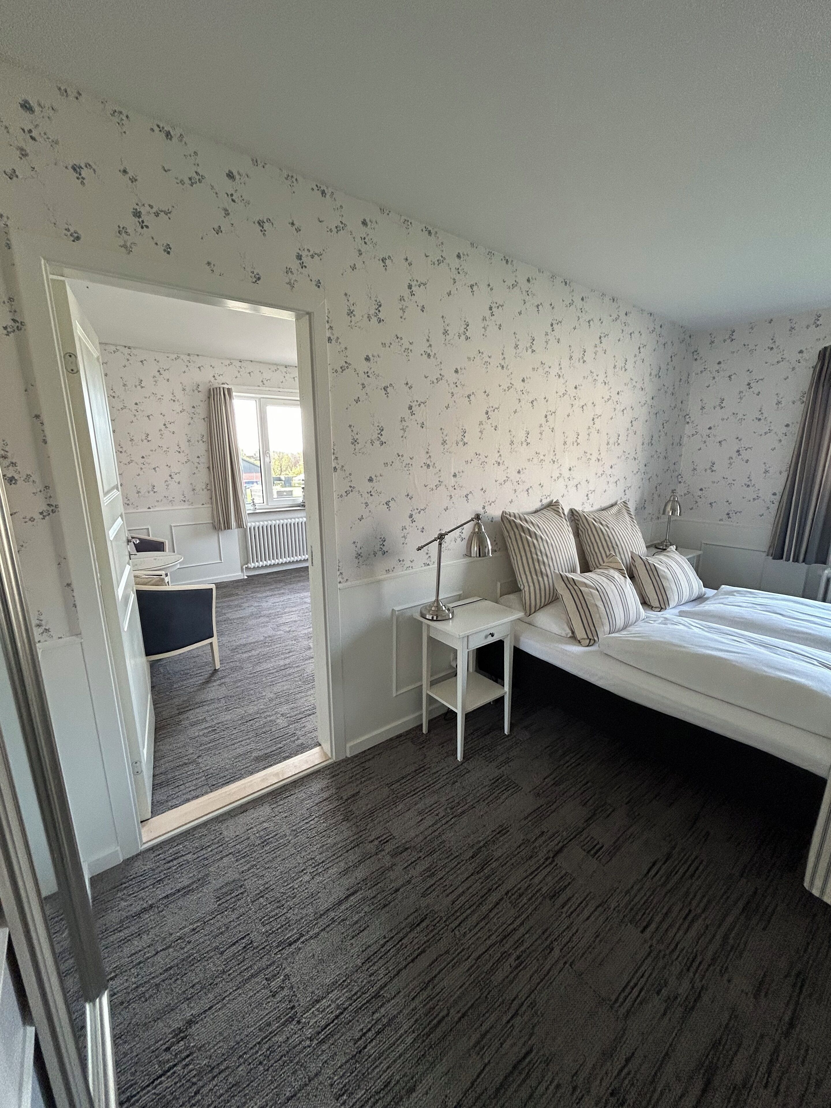 A bedroom with a bed, bedside table, lamp, and a view of a bathroom through an open door.