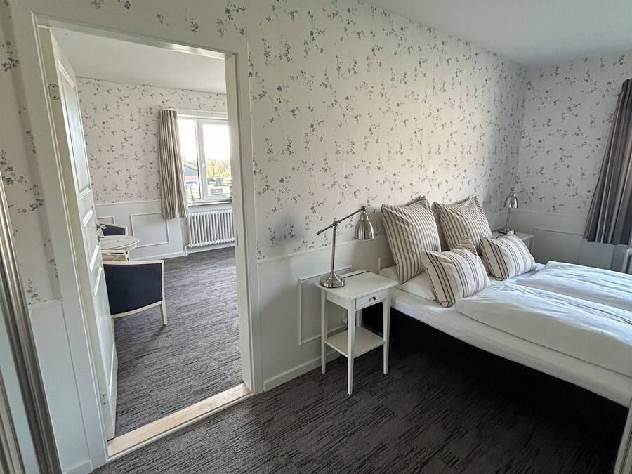 A bedroom with a bed, bedside table, lamp, and a view of a bathroom through an open door.