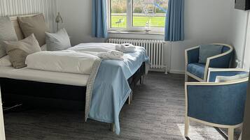 Un dormitorio con cama, una silla, un ventanal con vista a un parque infantil y un radiador.