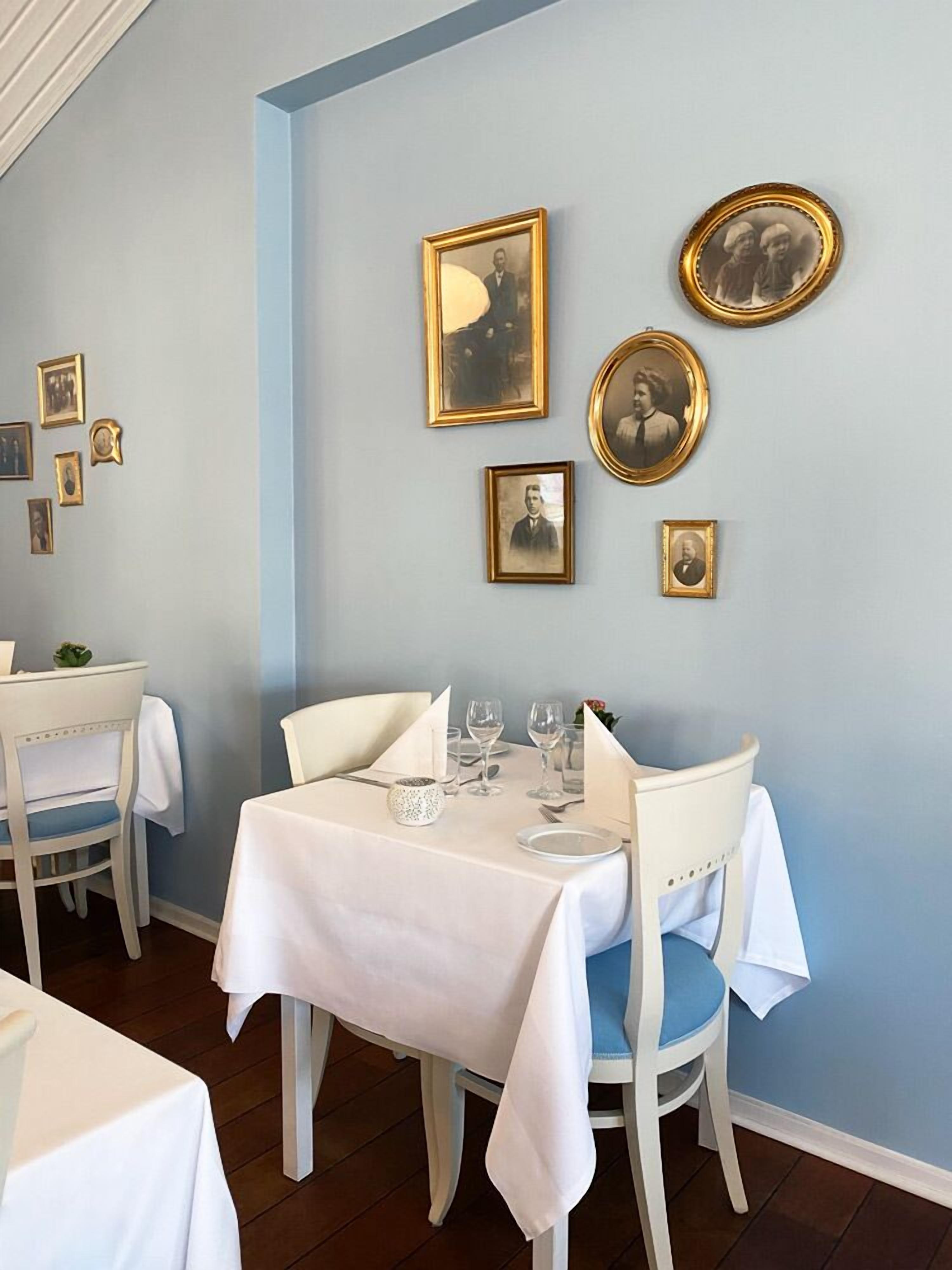 A dining area with a table set for two, chairs, and framed photographs on the wall.