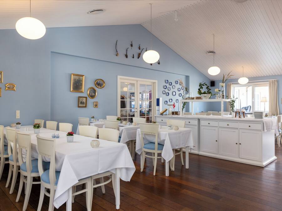 Un espace repas avec des tables et des chaises blanches, un comptoir de cuisine et diverses décorations murales.
