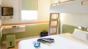Een hotelkamer met een stapelbed, een bureau met een stoel, een aan de muur bevestigde televisie en een raam dat natuurlijk licht binnenlaat.