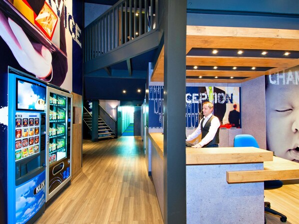 A modern interior with a reception desk, a staircase, and vending machines.