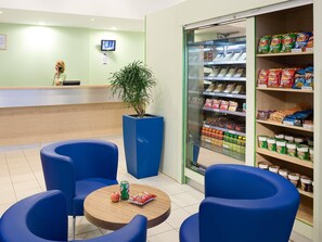 Een receptiegedeelte met een balie, een potplant en een koelkast vol snacks.