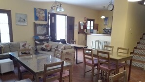 Un amplio salón con una mesa de comedor de vidrio rodeada de sillas de madera, un conjunto de sofás y una cocina al fondo.