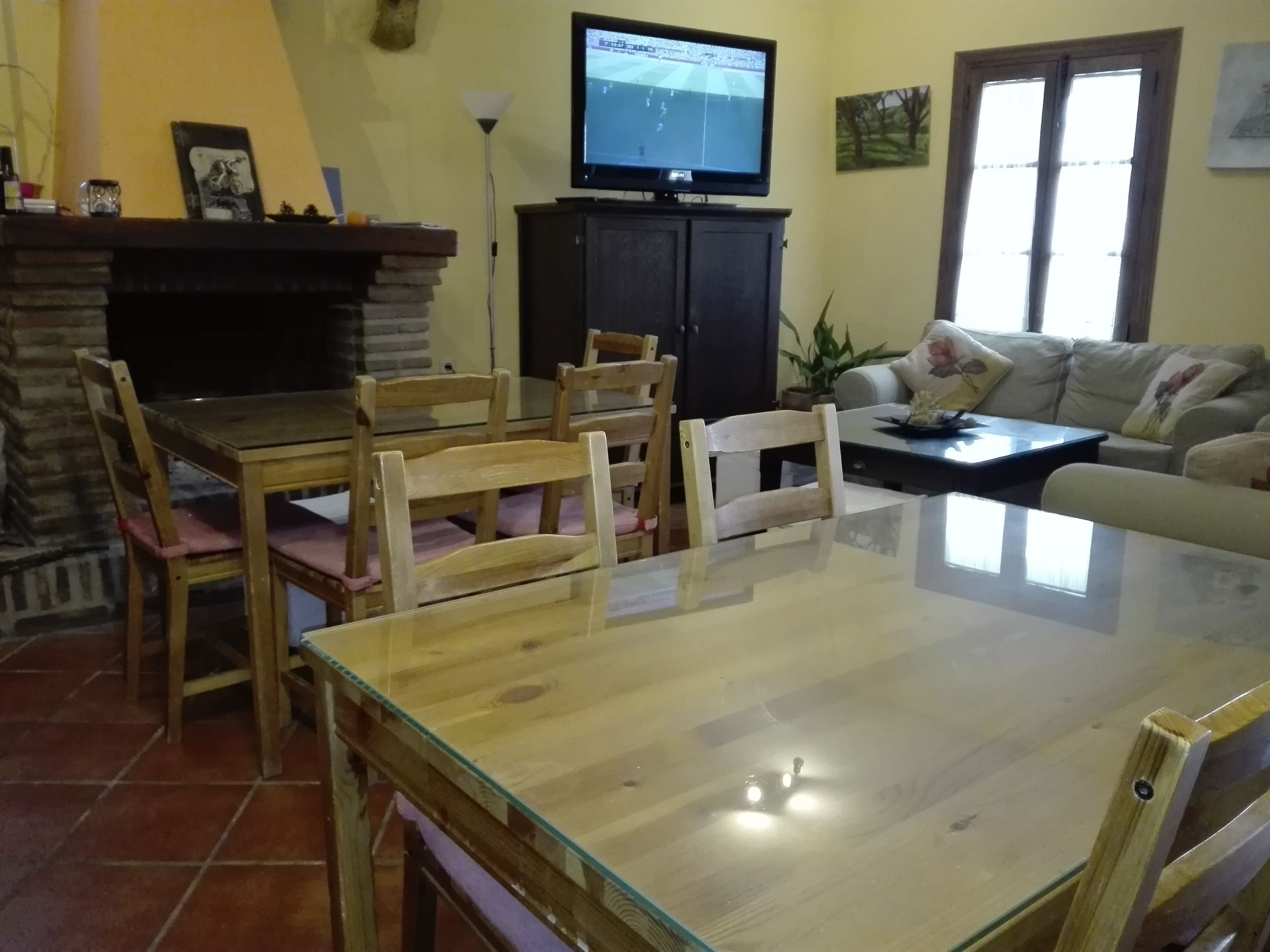 Un salon comprenant une table à manger avec un plateau en verre, des chaises en bois, un canapé, un téléviseur posé sur un meuble et une cheminée.