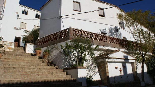 Un edificio blanco con un balcón, escalones de acceso y macetas con plantas.