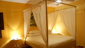 Una cama con dosel y cortinas blancas, una mesita de noche con lámpara y un cuadro en la pared.