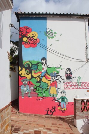 A colorful mural on a building's exterior featuring various characters and a tree. - Hostal La Posada del Recovero (Genalguacil)