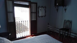 Un dormitorio con cama, una silla, una mesita, una ventana con vistas y un televisor de pared.