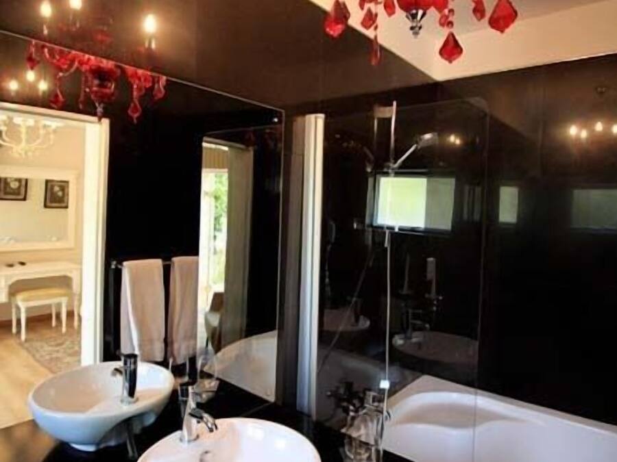 Un baño moderno con dos lavamanos, un espejo grande, una araña y una bañera.