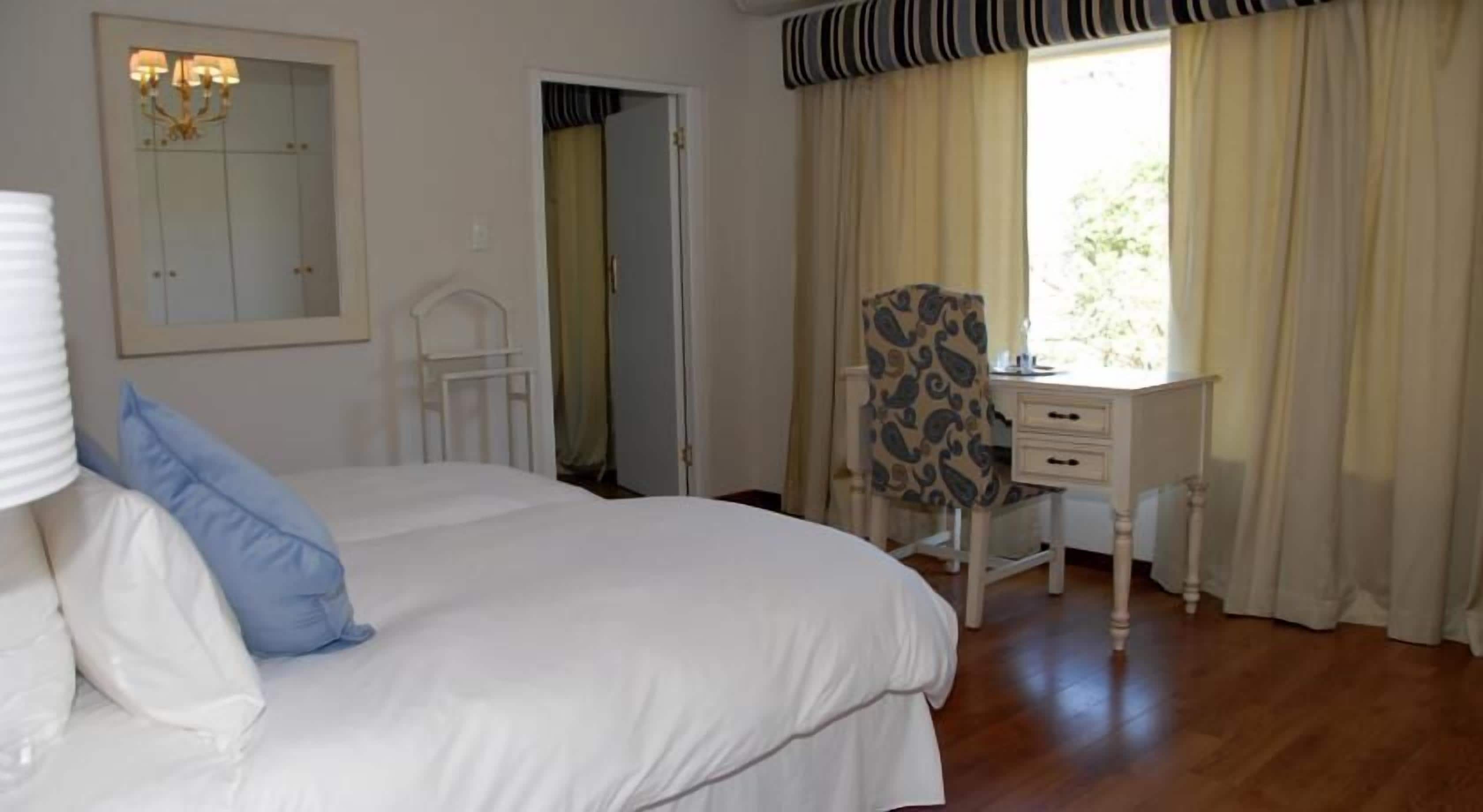 A bedroom with a large bed, a desk, and a chair. There is a mirror on the wall and a window with curtains.