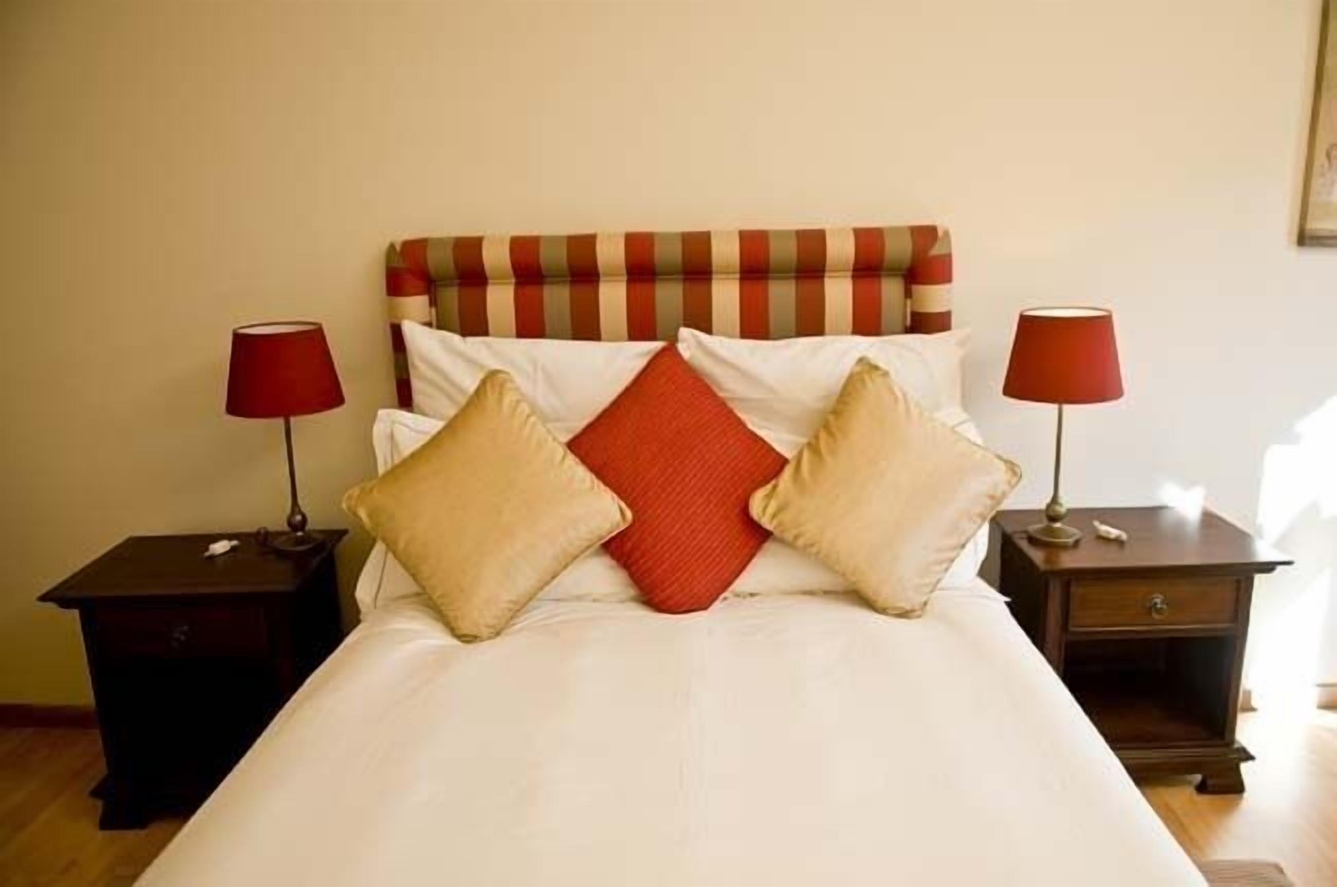 A neatly made bed with a striped headboard, two bedside tables with lamps, and a red pillow.