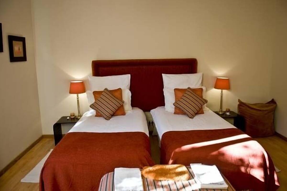A room with two beds, each with a red headboard, white bedding, and striped pillows. There are two bedside tables with lamps, and a small rug on the floor.