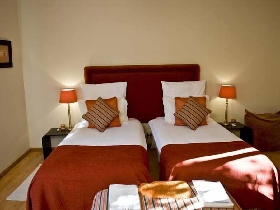 A room with two beds, each with a red headboard, white bedding, and striped pillows. There are two bedside tables with lamps, and a small rug on the floor.