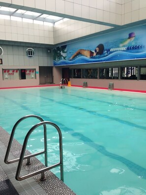 Una piscina interior con agua cristalina, una silla de salvavidas y un mural de un nadador.
