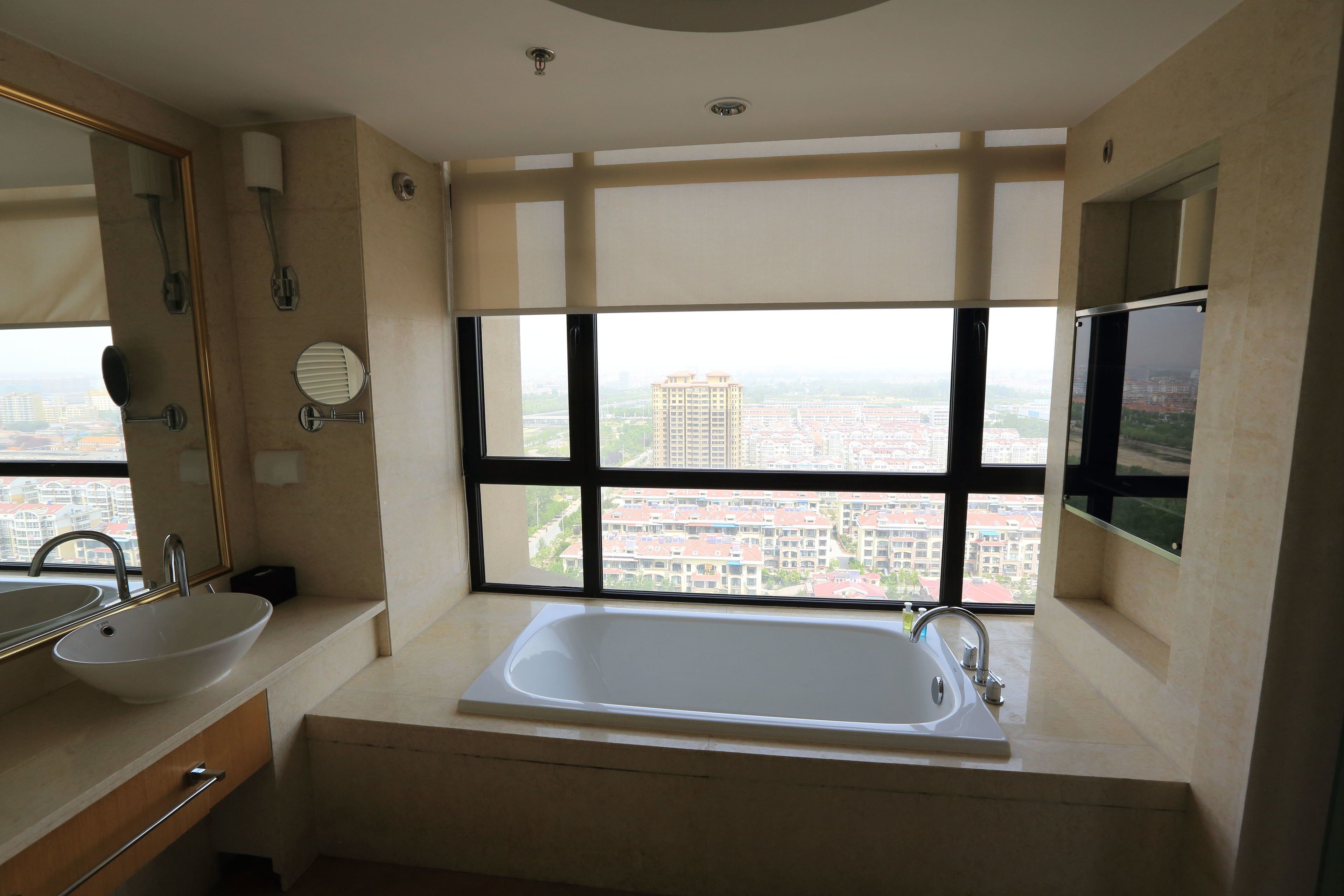 A modern bathroom with a large window, a bathtub, and a sink.