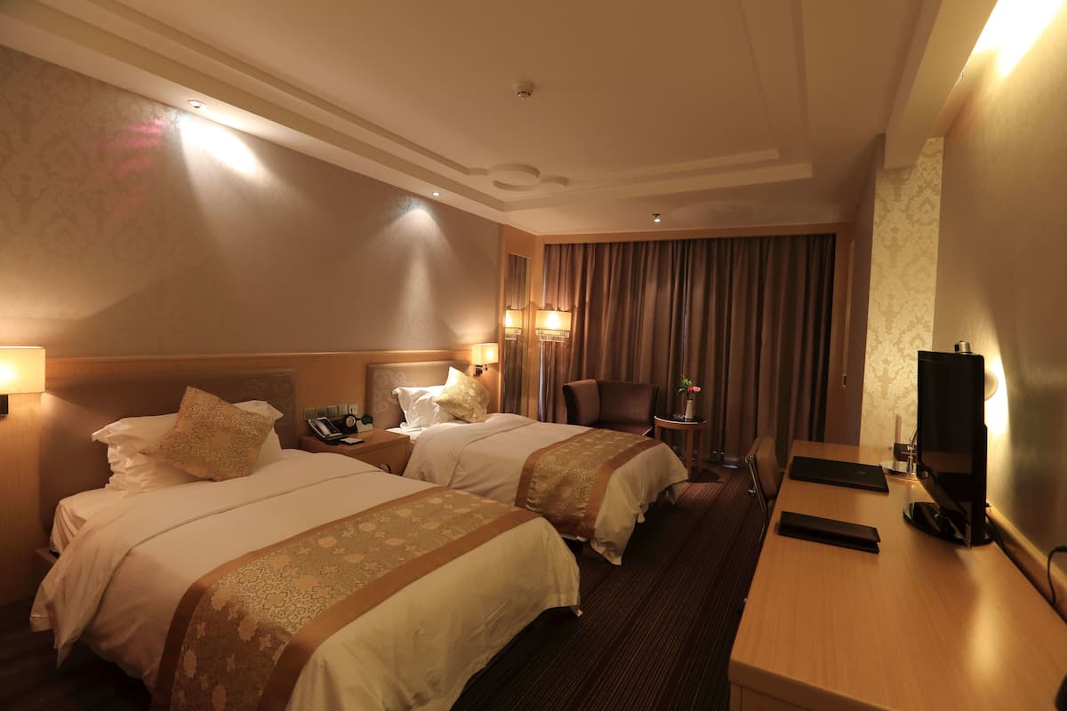 Habitación de hotel con dos camas, un escritorio, una silla, un televisor y una lámpara.