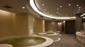 Un moderno espacio de spa con varias tinas de hidromasaje y una tina central grande, rodeado de paredes color beige y un techo curvo con iluminación empotrada.