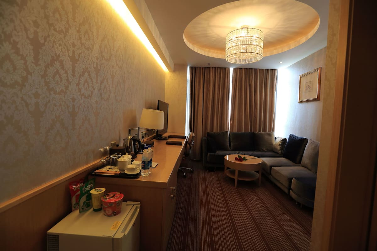 Habitación de hotel con kitchenette, un sofá, una pequeña mesa redonda y un amplio ventanal con cortinas.