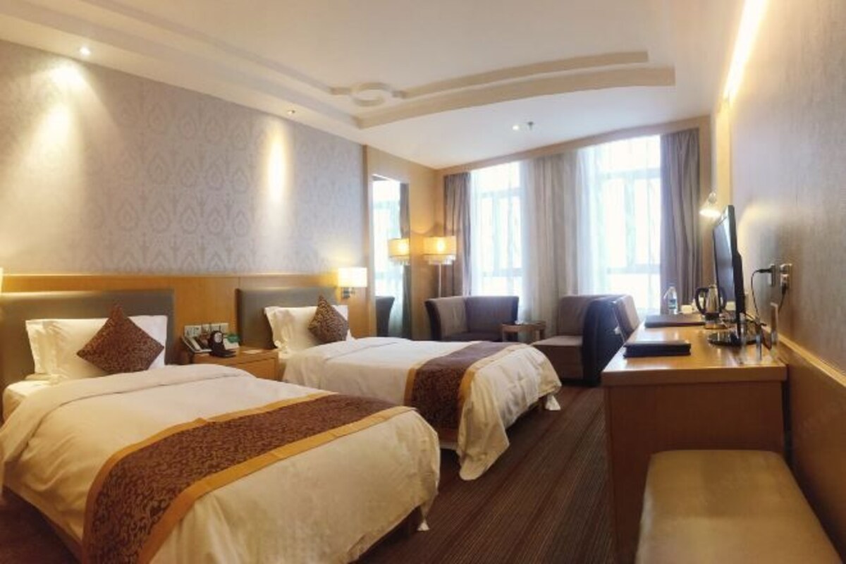 A hotel room with two beds, a desk, a chair, and a TV.
