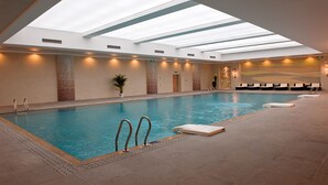 Una piscina interior con techos de vidrio transparente, sillas de descanso y una planta en maceta.