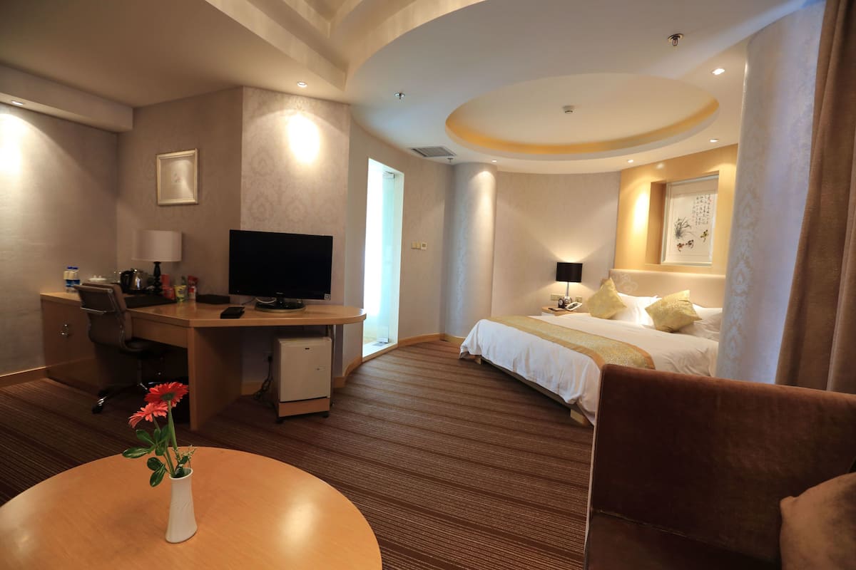 Una habitación de hotel con cama, escritorio, silla, televisor y un florero con flores.