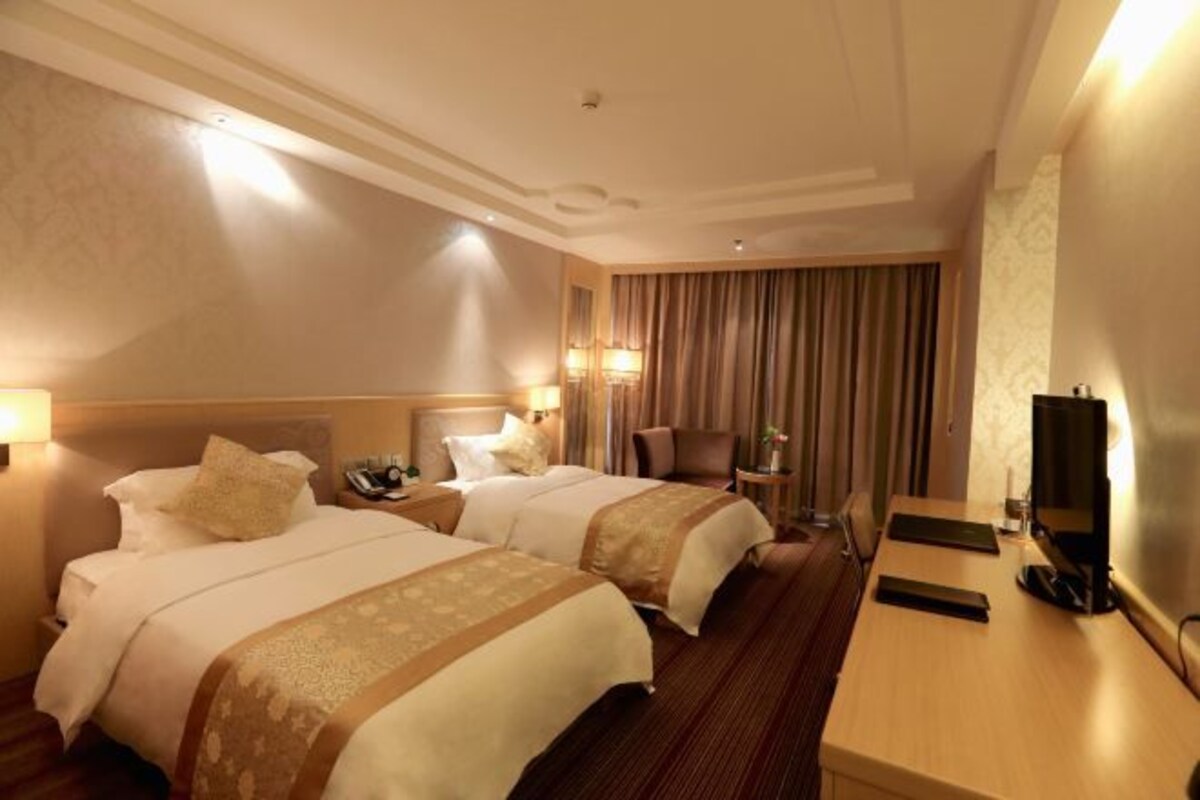 Une chambre d’hôtel avec deux lits, un bureau, une chaise, une télévision et une fenêtre avec des rideaux.