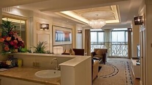 Una habitación de hotel moderna con un amplio tocador de baño, una araña, un balcón con barandilla y un gran ventanal.