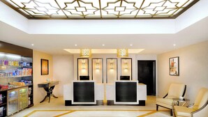 Uma área de recepção de hotel com design moderno, com balcão de atendimento, espaço de estar e um quiosque de bebidas.