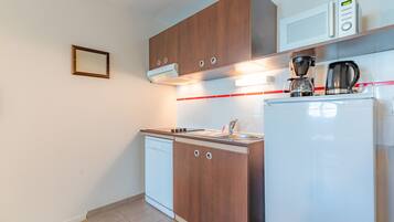 A compact kitchen with wooden cabinets, a white dishwasher, a coffee maker, and a microwave.