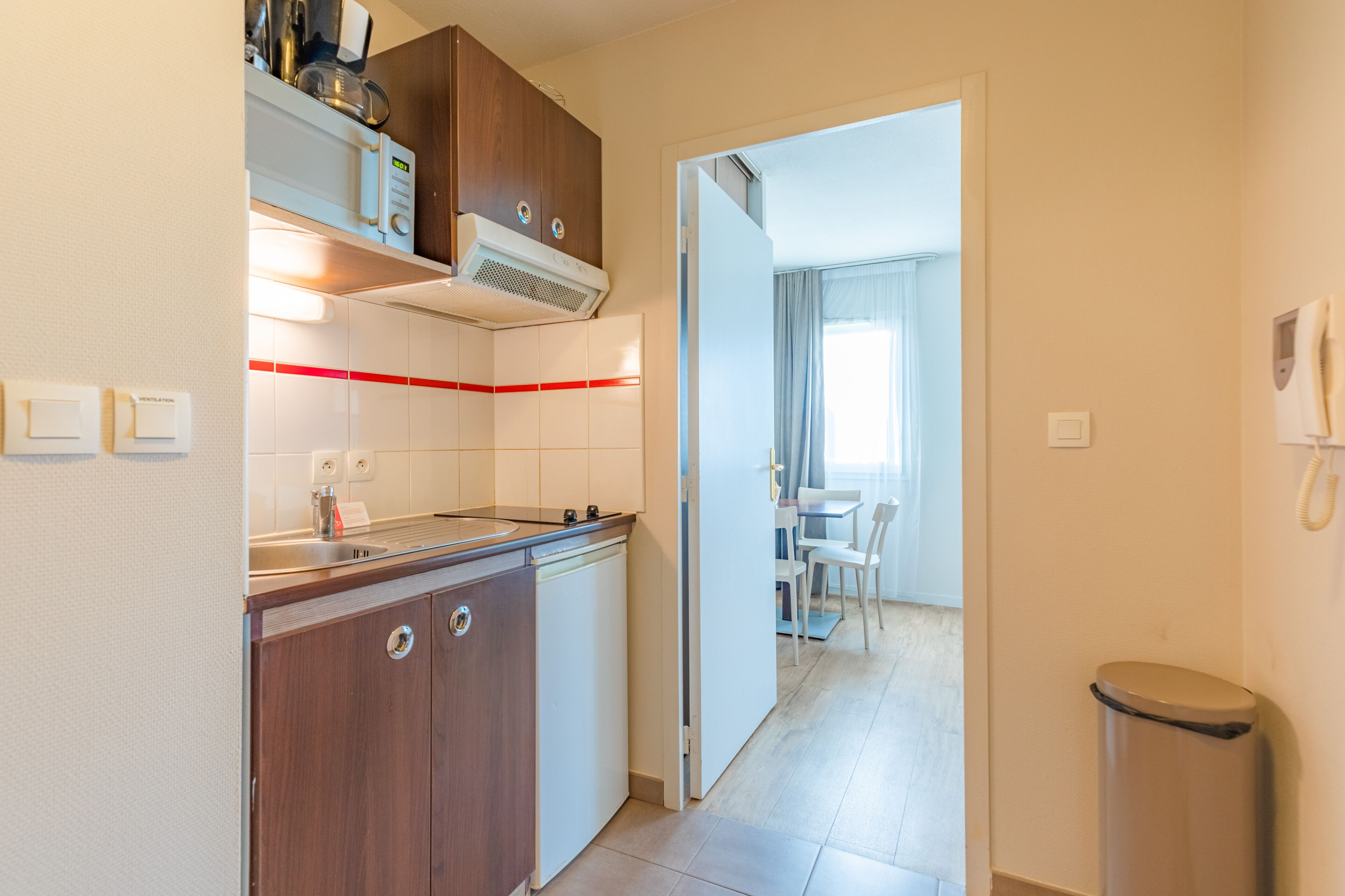 A compact kitchen with a stove, sink, and cabinets, leading to a dining area with a table and chairs.