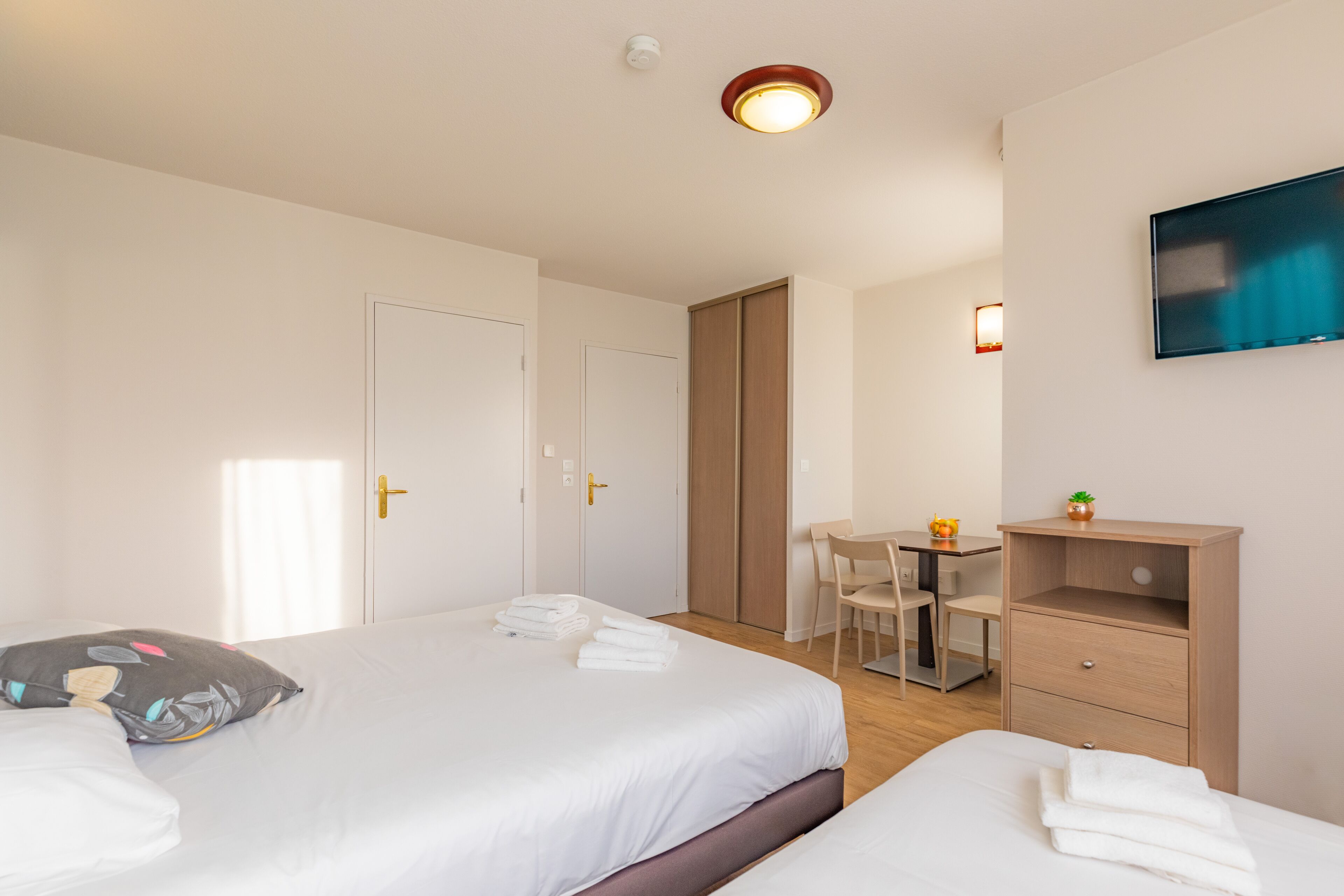 A hotel room with two beds, a desk, a chair, and a TV mounted on the wall.