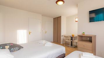 A hotel room with two beds, a desk, a chair, and a TV mounted on the wall.