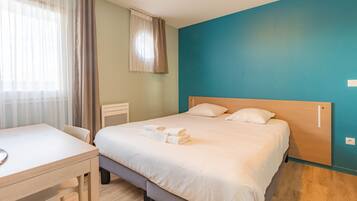 A hotel room with a bed, a desk, and a window with curtains.