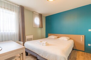 Quarto de hotel com cama, escrivaninha e janela com cortinas.