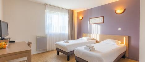 A hotel room with two beds, a desk with a computer, and a window with curtains.