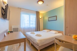 Una habitación de hotel con cama, mesita de noche, silla y una pequeña mesa con fruta.