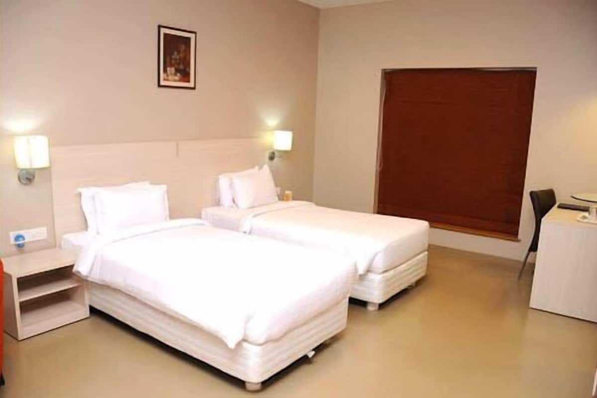 A hotel room with two beds, a nightstand, a desk, and a window with blinds.