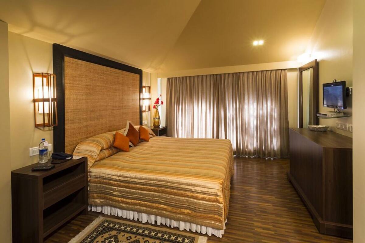 A hotel room with a large bed, a wooden nightstand, a TV, and a desk with a computer.