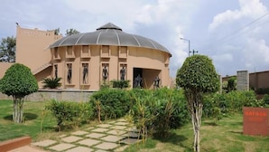 Un bâtiment doté d’une structure en forme de dôme, entouré d’un espace verdoyant bien entretenu et d’un chemin pavé menant à l’entrée.