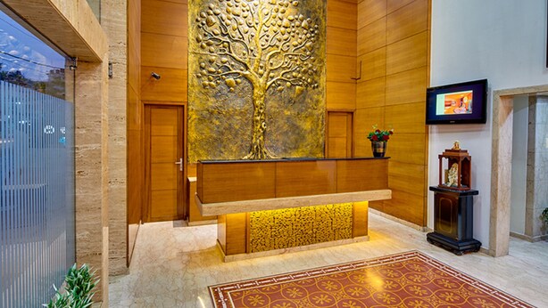 A reception area with a large tree mural, a wooden bench, a TV, and a patterned carpet. - Coraltree By Goldfinch Hotels Bangalore (Bengaluru)