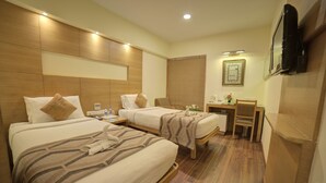 A hotel room with two beds, a desk, a chair, a TV, and a picture on the wall. - Coraltree By Goldfinch Hotels Bangalore (Bengaluru)