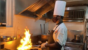 A chef cooking with a large flame on a stove in a professional kitchen. - Coraltree By Goldfinch Hotels Bangalore (Bengaluru)