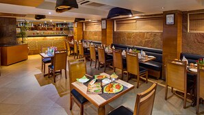 A restaurant with booths and tables, a bar area, and a stone wall. - Coraltree By Goldfinch Hotels Bangalore (Bengaluru)