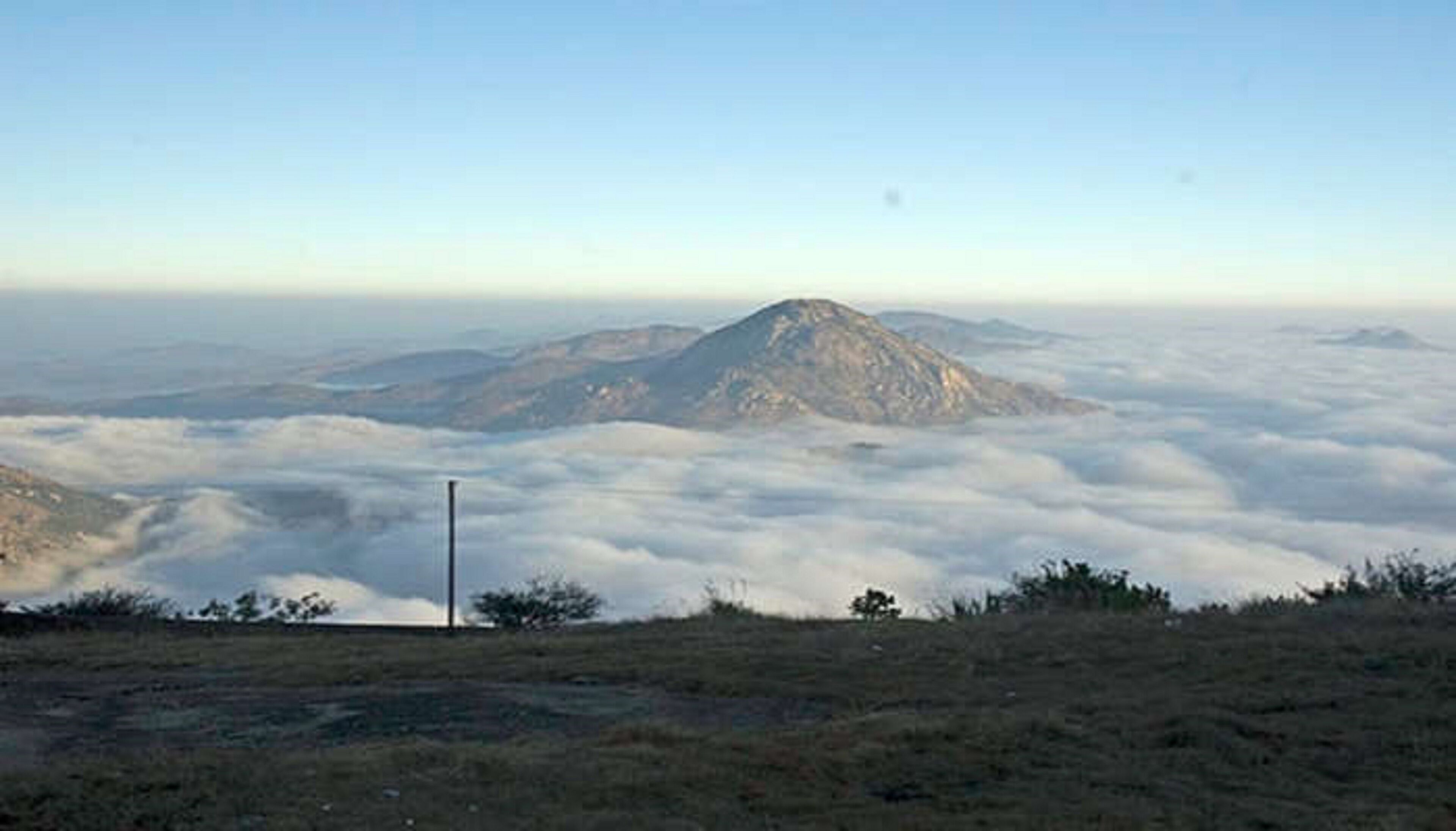 A mountain landscape with a clear view of the clouds below and a white pole in the foreground.