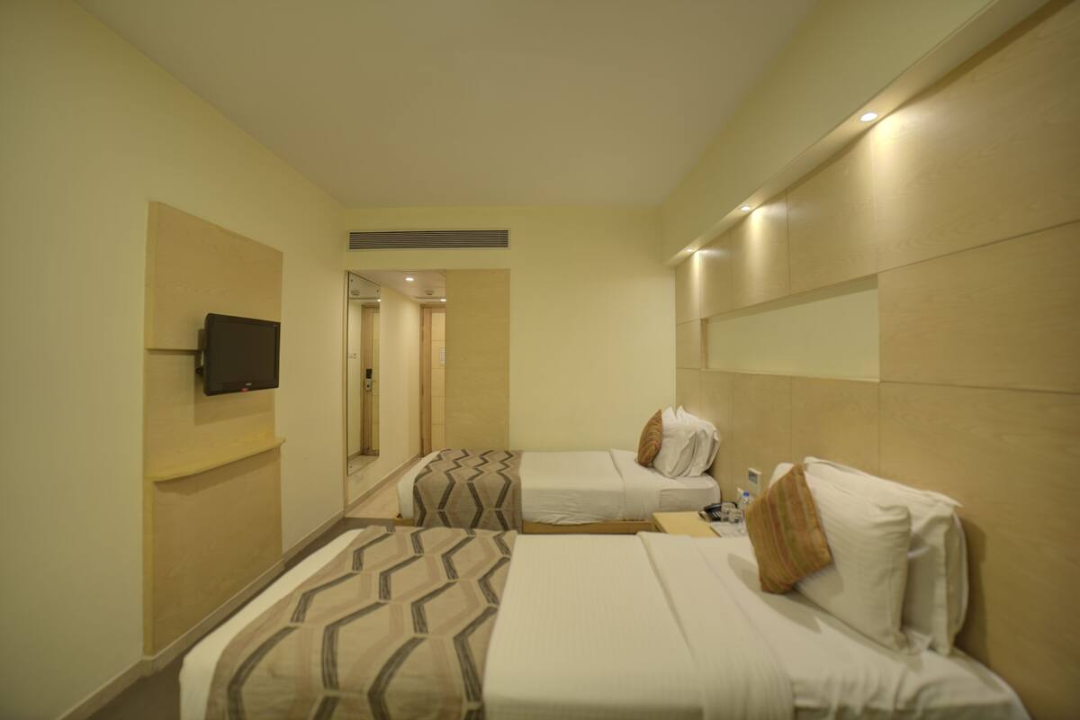 Habitación de hotel con dos camas, un televisor montado en la pared y un espejo.
